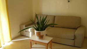 A living room with a beige sofa, a small wooden table with a potted plant, and a yellow curtain. - Philippos Studios & Apartments (Kos)