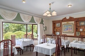 Un comedor con varias mesas y sillas, una araña y cuadros en las paredes.