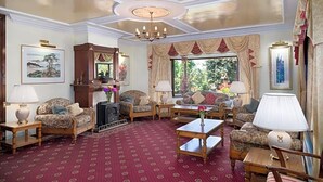 A room with a patterned carpet, a chandelier, and multiple sofas and armchairs arranged around a central coffee table. - Kathleens Country (Killarney)