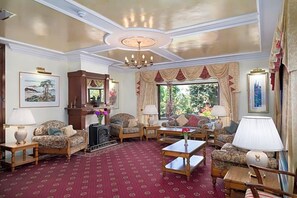 Una habitación con alfombra estampada, un candelabro y varios sofás y sillones dispuestos alrededor de una mesa de centro.