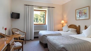 A hotel room with two beds, a desk with a chair, a TV mounted on the wall, and a window with curtains. - Kathleens Country (Killarney)