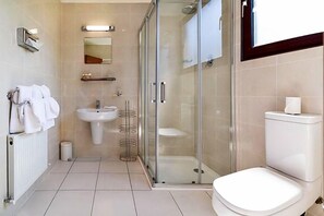 Un baño moderno con ducha envuelta en vidrio, un lavamanos blanco y un inodoro.