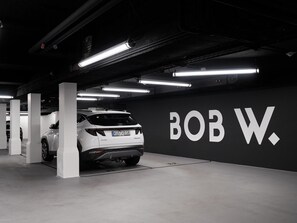 A parking garage with a white SUV parked in a spot marked with the number 22. The wall features large white letters spelling 'BOB W.' - Hotello Schwabing (Munich)