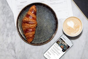 En croissant på en tallrik, en kopp kaffe och en meny med olika frukostalternativ.