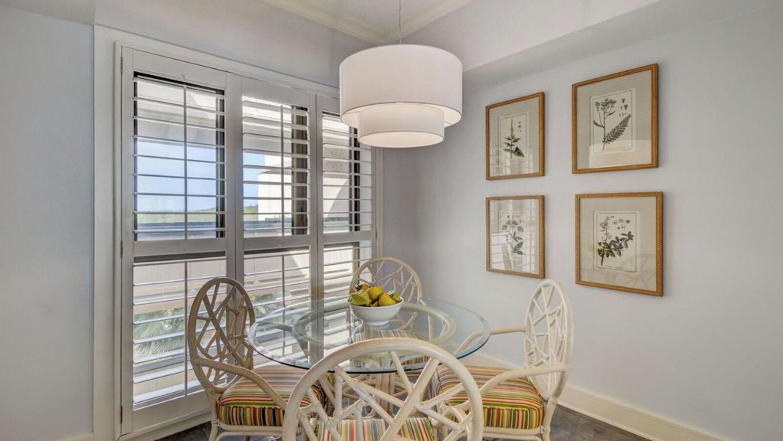 A dining area with a glass table, wicker chairs, and a white pendant light.