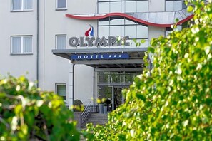 Un hotel llamado 'OLYMPIC HOTEL' con un diseño moderno, que presenta un logotipo destacado y una escalera que conduce a la entrada.