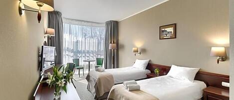 A hotel room with two beds, a desk, a chair, a small table, and a window with curtains.