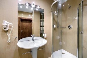 A bathroom with a white sink, a glass shower enclosure, and a hairdryer on the wall. - Land-gut-hotel Olympic (Wronki)