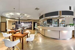 A modern bar area with a curved counter, white bar stools, and pendant lighting. - Land-gut-hotel Olympic (Wronki)