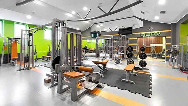 A gym with various exercise equipment, a weight bench, and a wall-mounted TV. - Land-gut-hotel Olympic (Wronki)