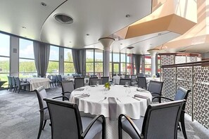 A conference room with round tables, chairs, and a large window offering a view of greenery. - Land-gut-hotel Olympic (Wronki)