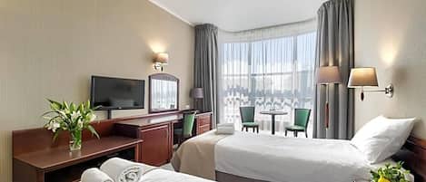 A hotel room with two beds, a desk, a television, and a view of the city.
