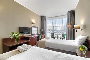 A hotel room with two beds, a desk, a television, and a view of the city. - Land-gut-hotel Olympic (Wronki)