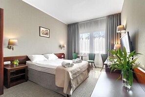 A hotel room with a bed, bedside tables, a desk, a chair, a lamp, a picture on the wall, and a plant. - Land-gut-hotel Olympic (Wronki)