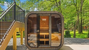 Una cabaña de madera con puerta de vidrio, una escalera de madera y un banco en el exterior.