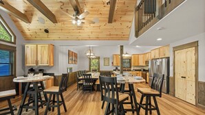 Un comedor amplio con mesas y sillas de madera, un ventilador de techo y vistas a la cocina.