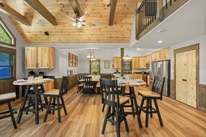 A spacious dining area with wooden tables and chairs, a ceiling fan, and a view of the kitchen. - Wet Yeti by PMR with Indoor Pool, Game Room, Sauna, Hot Tub, Fire Pit (Lake Harmony)