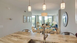Un espace repas doté d’un îlot en marbre, de luminaires suspendus, de chaises en osier et offrant une vue dégagée grâce à de grandes fenêtres.