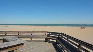 Une terrasse en bois qui mène à une plage de sable et offre une vue dégagée sur l’océan.