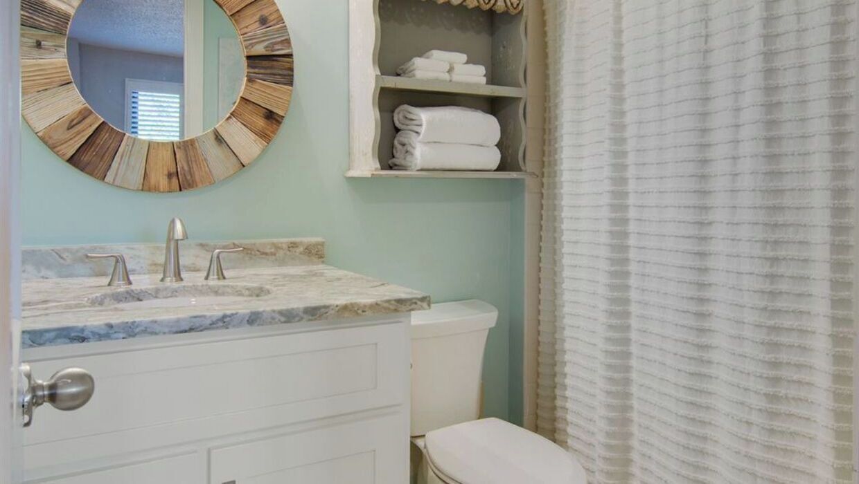 A bathroom with a marble sink, a toilet, a round mirror, and a towel shelf.
