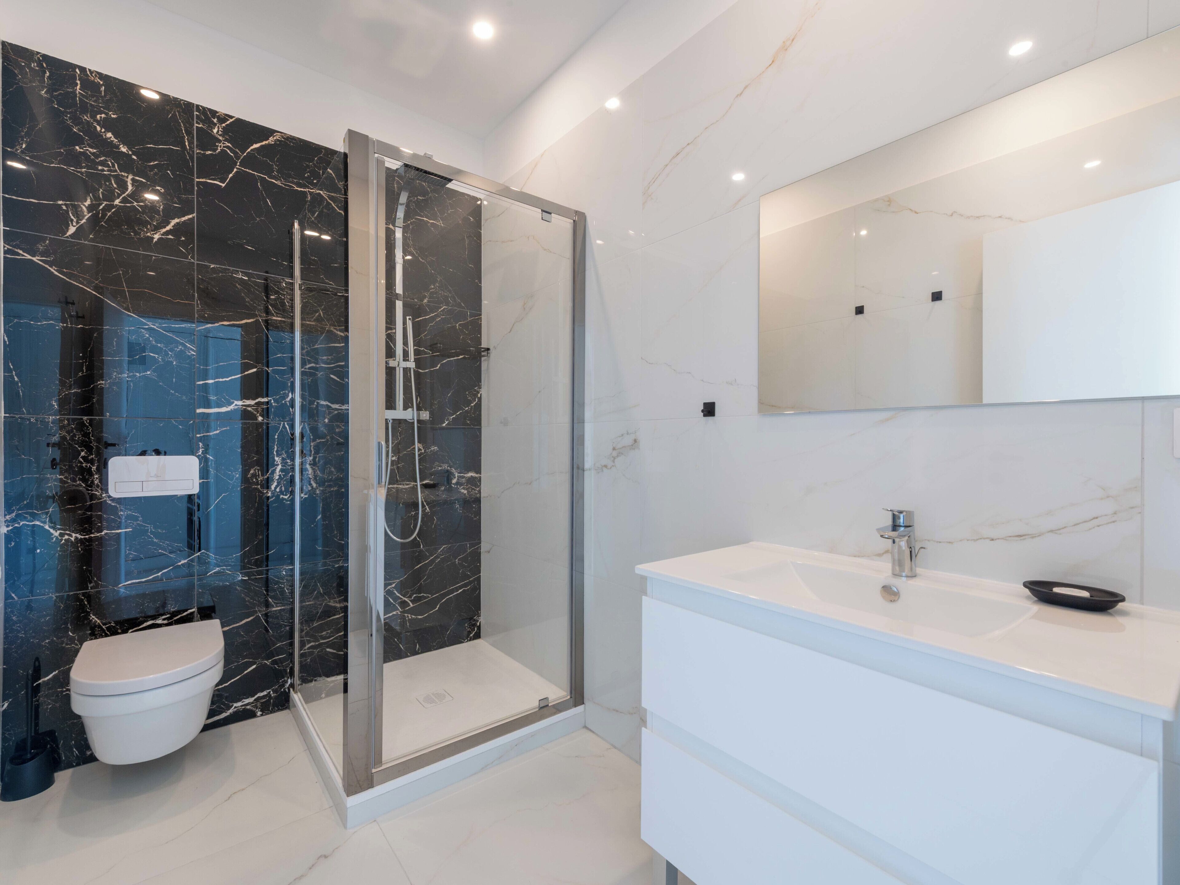 Un baño moderno con ducha envuelta en vidrio, un lavamanos blanco y pared revestida de mármol.