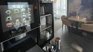 A modern living room with a coffee machine, a bookshelf, and a dining area with a table and chairs. - Stadt-gut-hotel Astra (Ulm)