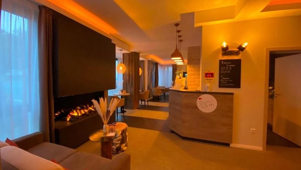 A hotel lobby with a sofa, a fireplace, a reception desk, and a large screen. - Stadt-gut-hotel Astra (Ulm)