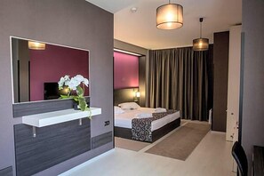 A modern hotel room with a large bed, a bedside table, a mirror, and a hanging light fixture. - Hotel Idol (Targovishte)
