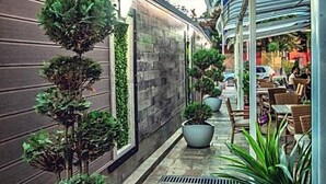 A narrow outdoor corridor with potted plants, stone flooring, and a modern building with large windows. - Hotel Idol (Targovishte)