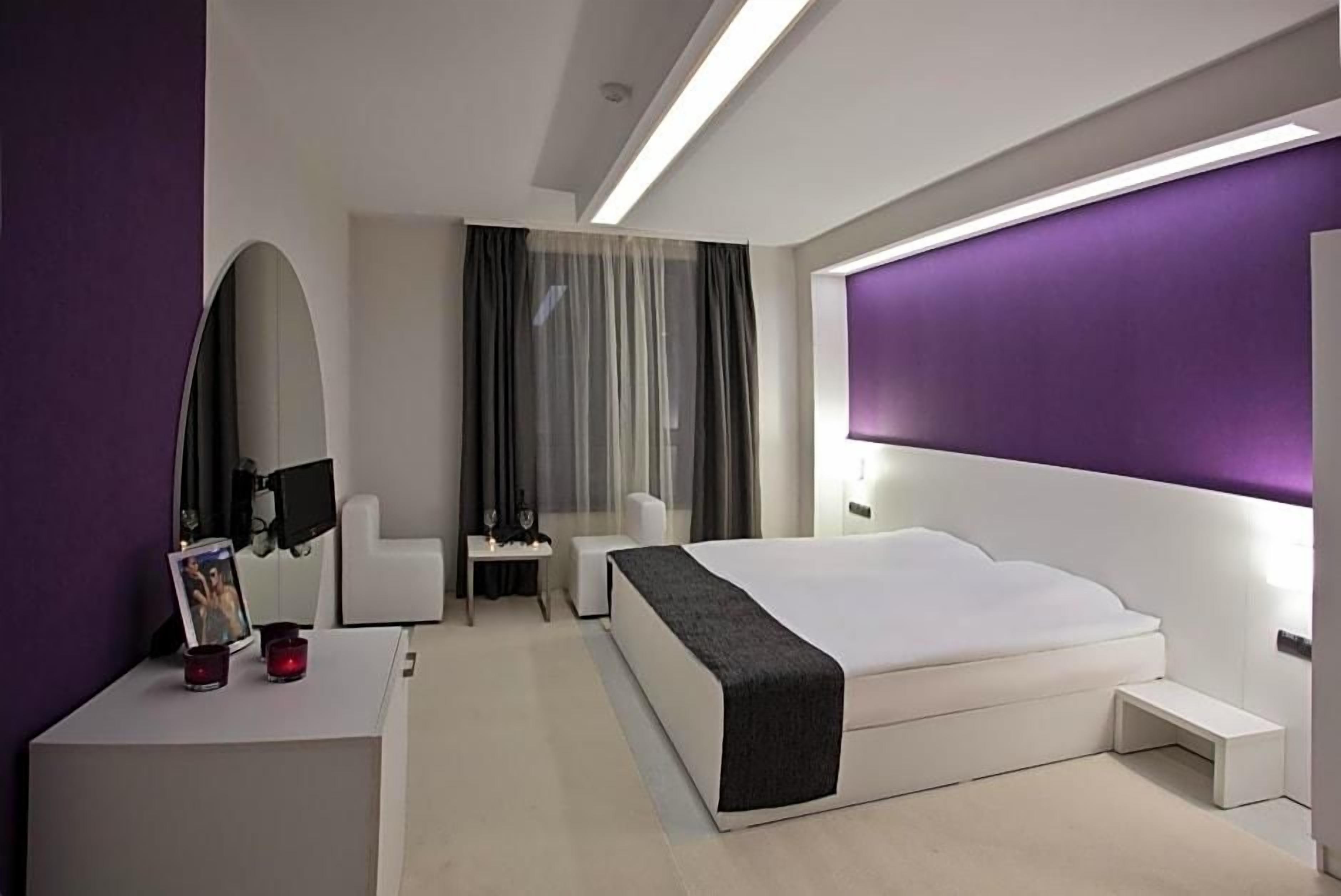 Ein modernes Hotelzimmer mit einem großen Bett, einem Nachttisch, einem Sessel, einem Schreibtisch und einem großen Spiegel.