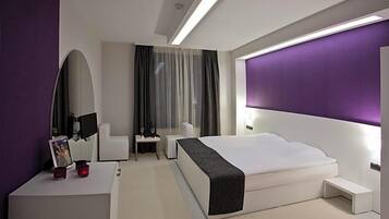 Habitación de hotel moderna con una cama grande, una mesita de noche, una silla, un escritorio y un espejo amplio.