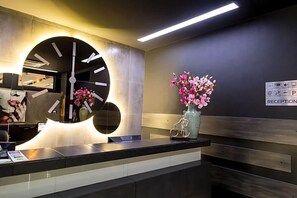 A reception area with a large clock, a vase of flowers, and a sign indicating a reception desk. - Hotel Idol (Targovishte)