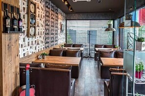 A restaurant interior with wooden tables and booths, a wall with clocks, and large windows. - Hotel Idol (Targovishte)