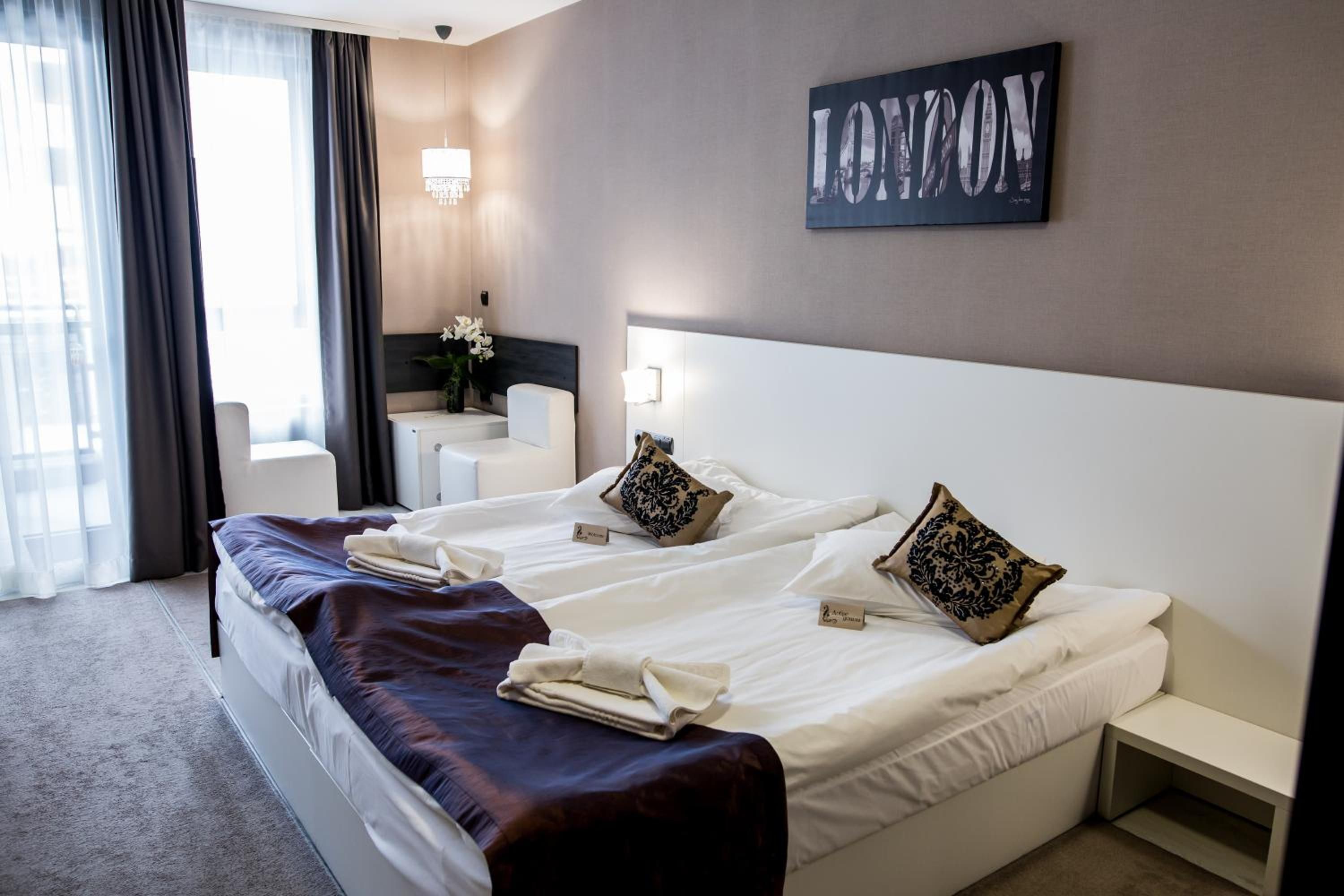 Habitación de hotel con dos camas, una mesita de noche, una silla, una lámpara y una obra de arte colgada en la pared.
