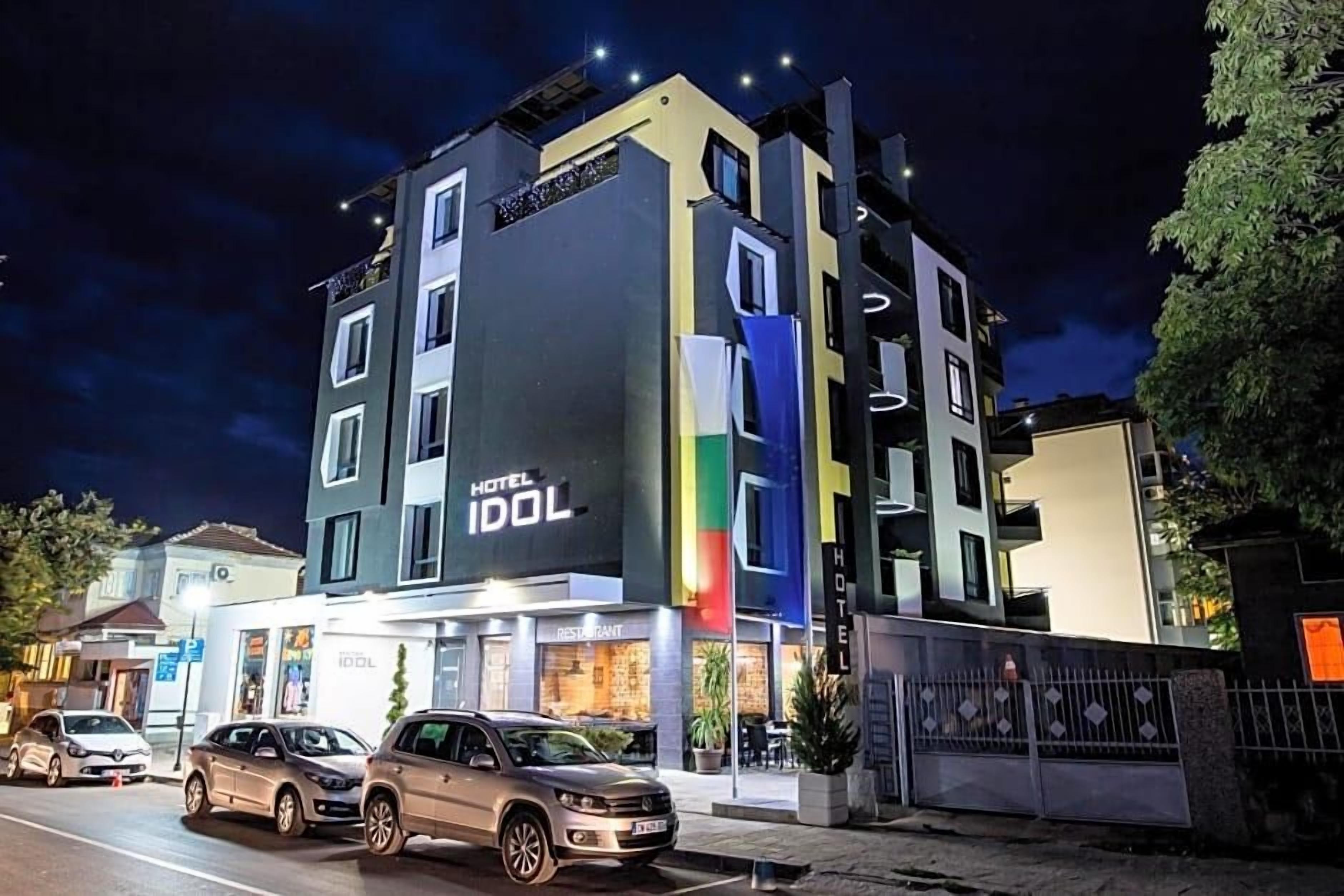 Un hotel de varios pisos con un letrero llamativo que dice 'HOTEL IDOL', un restaurante y una entrada con portones.