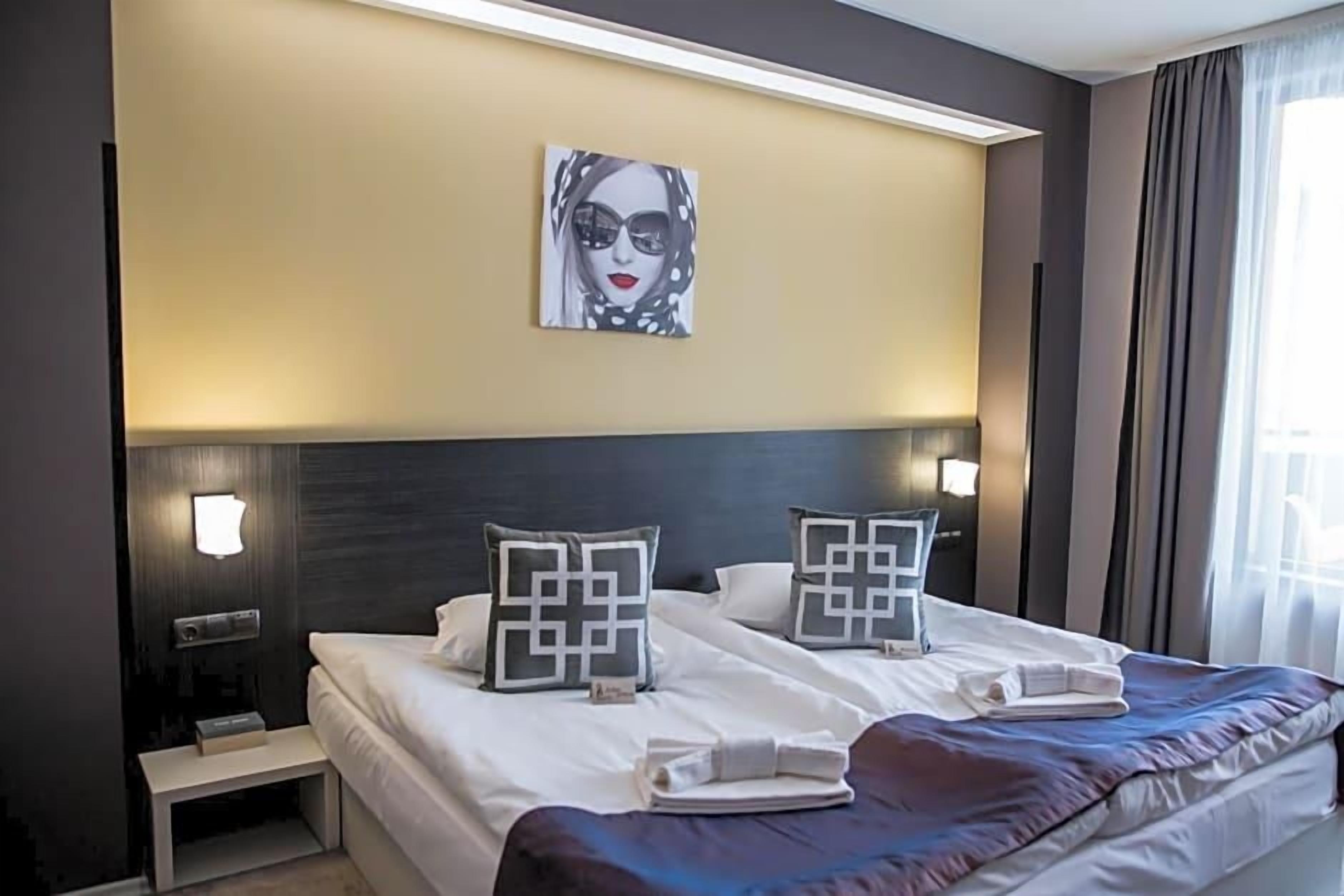 A hotel room with a large bed, two bedside tables, a wall-mounted artwork, and a window with curtains.