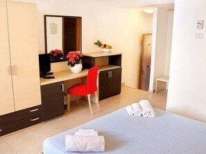 A hotel room with a bed, a desk with a chair, a mirror, a bowl of fruit, and a vase with flowers. - Villagio La Darsena (Scarlino)