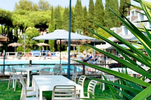 A pool area with lounge chairs and umbrellas, surrounded by greenery. - Villagio La Darsena (Scarlino)