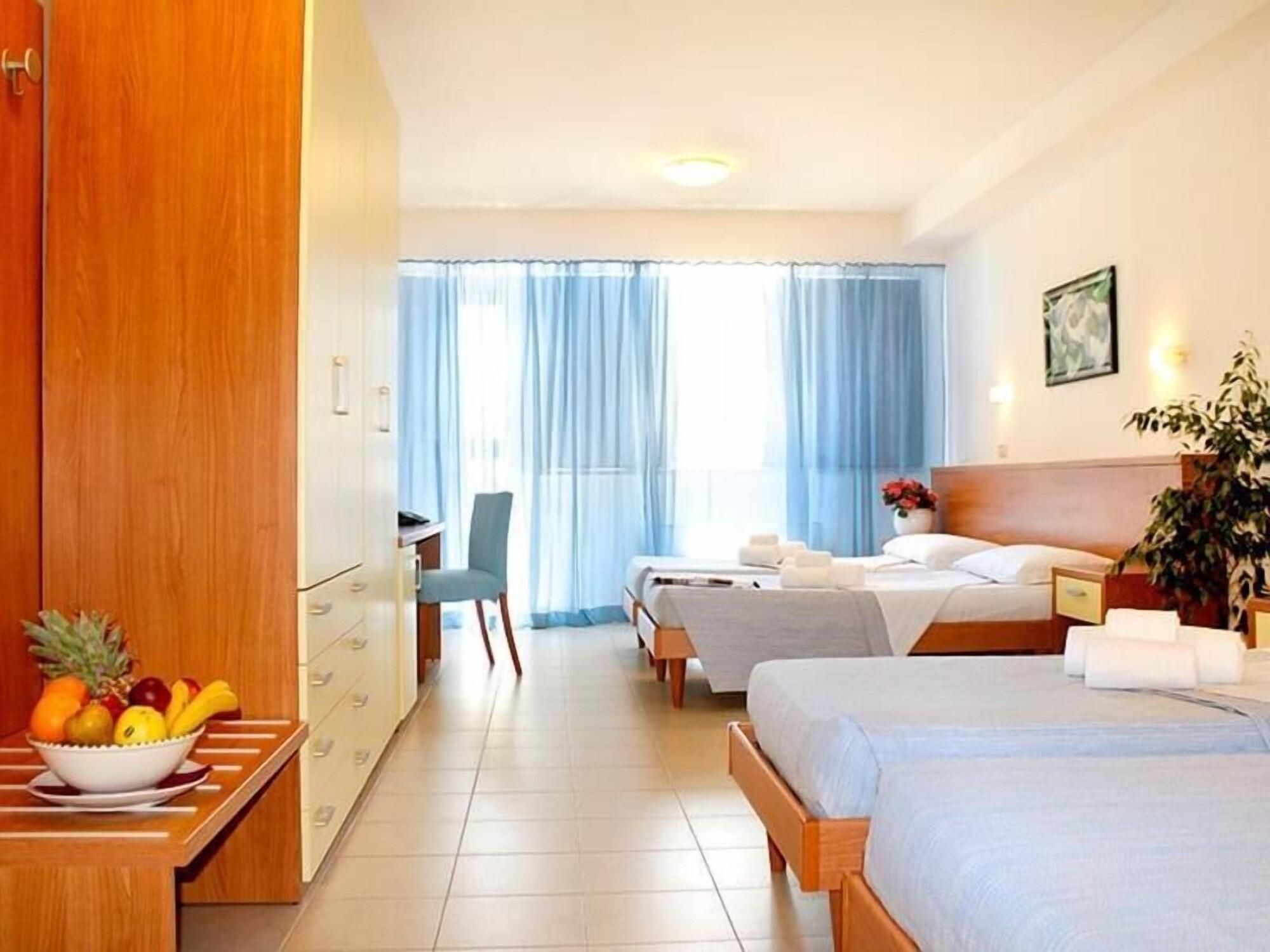 Camera d'albergo con due letti, una scrivania, una sedia, una ciotola di frutta e una pianta in vaso.