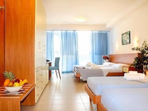 A hotel room with two beds, a desk, a chair, a fruit bowl, and a potted plant. - Villagio La Darsena (Scarlino)