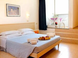 Habitación de hotel con cama, bandeja de desayuno, un cuadro y vistas al exterior.