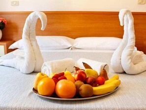 A hotel room with a bed, pillows, and a fruit and towel arrangement on the bed. - Villagio La Darsena (Scarlino)