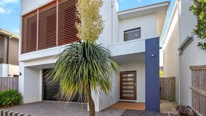 Una casa moderna de dos pisos con garaje, un pequeño jardín con una palmera y un cerco de madera.
