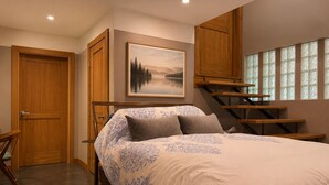 A bedroom with a bed, a painting, a staircase, and a door.