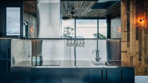 A modern kitchen with stainless steel appliances, wooden accents, and a view through large windows.