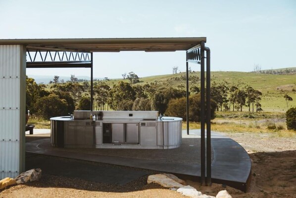 An outdoor kitchen area with a built-in stove and sink, set against a backdrop of a grassy landscape and hills.