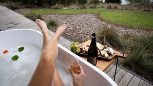 A bathtub with a wooden deck, a bottle of wine, and a fruit platter.
