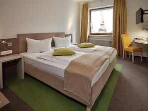 Hotellihuone, jossa on sänky, yöpöytä, tuoli ja televisio.