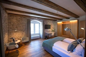 Ein Schlafzimmer mit Bett, Schreibtisch, Stuhl, Fernseher und einer Steinwand.