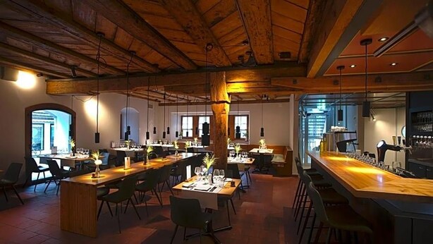 A spacious dining area with multiple tables and chairs, wooden beams on the ceiling, and a bar counter. - Gasthaus Zum Trauben (Weinfelden)